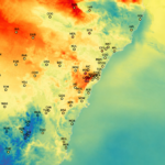 Colour-shaded map of eastern New South Wales showing modelled near-surface air temperatures. Warm colours (yellow, orange and red) dominate inland areas and the Sydney region, while cooler greens and blues occur along the coast and across the elevated terrain of the Snowy Mountains in the south-west. Weather station locations are marked by labelled circles distributed across the map, with a dense cluster around Sydney. The Tasman Sea appears on the right in pale blue-green shades, and the map focuses solely on the geographic region without axes, title, or legend.