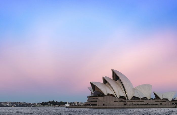The distinctive white sails of Sydney Opera House in the bottom right, with a pink and blue sky behind